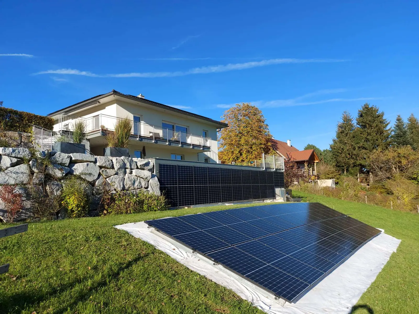Wohnhaus mit PV-Zaun und Freiflächenanlage bei blauem Himmel